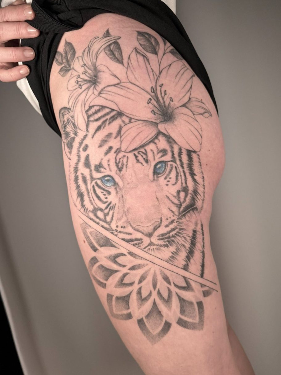 Tattoo eines Tigers mit blauen Augen und Blumen auf dem Oberschenkel  – gestochen im Fineline und Dotwork Stil in Neu-Ulm bei Ink Shell