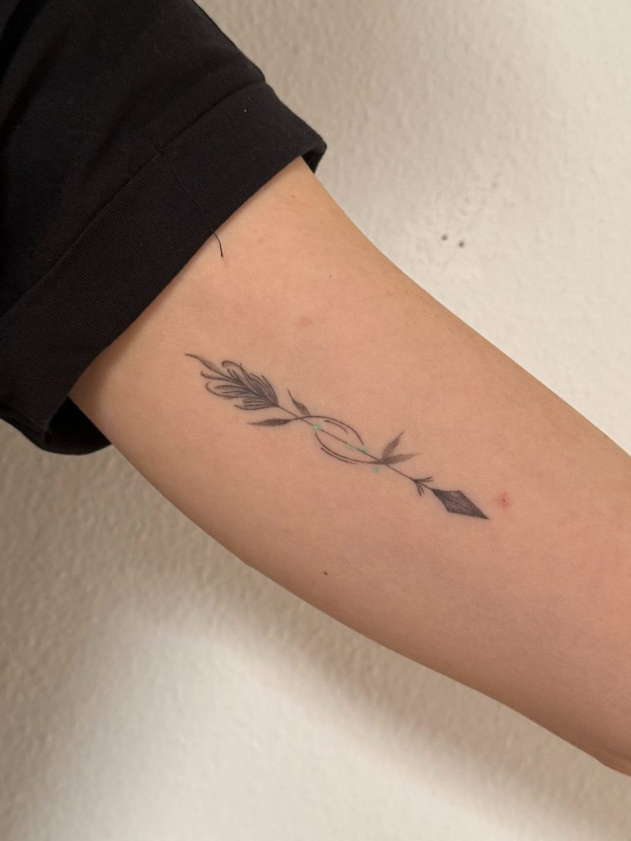 Schwarzes Tattoo eines stilisierten, geometric, fineline Pfeil auf einem Arm – Michelle Klein, Rabauke Studio, Neu-Ulm